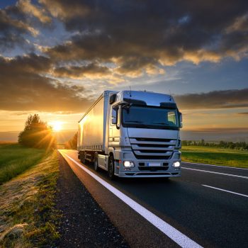 Truck driving on the asphalt road in rural landscape at sunset with dark clouds